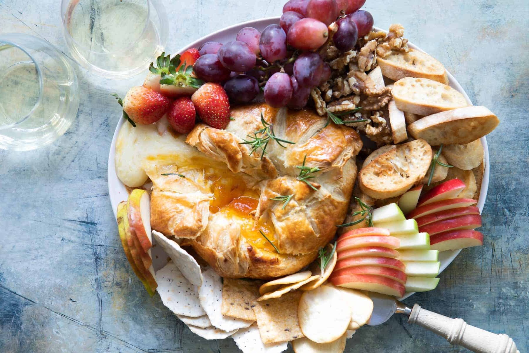 A platter with fruits, crackers and nuts with baked brie in puff pastry in the middle.