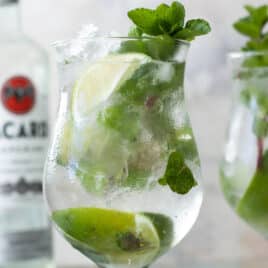 Two mojito cocktails in glasses with a bottle of white rum in the background.
