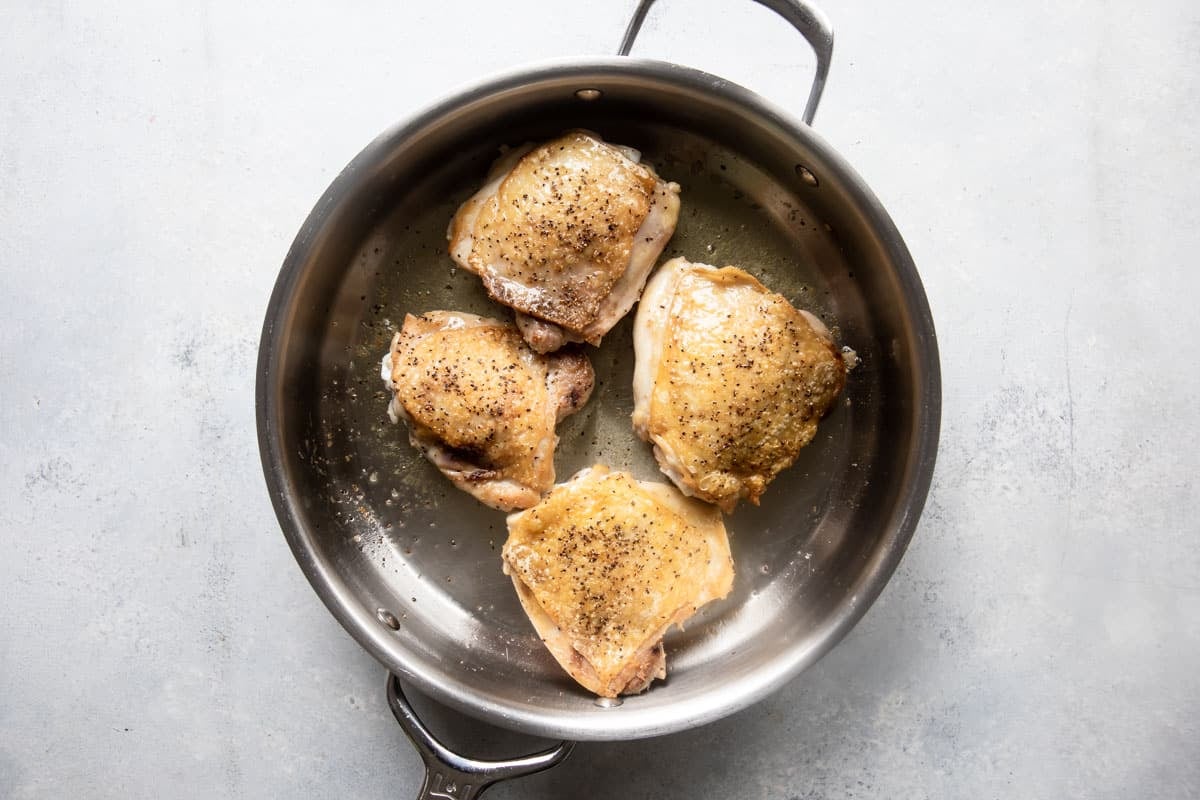 Chicken thighs being cooked in a skillet.