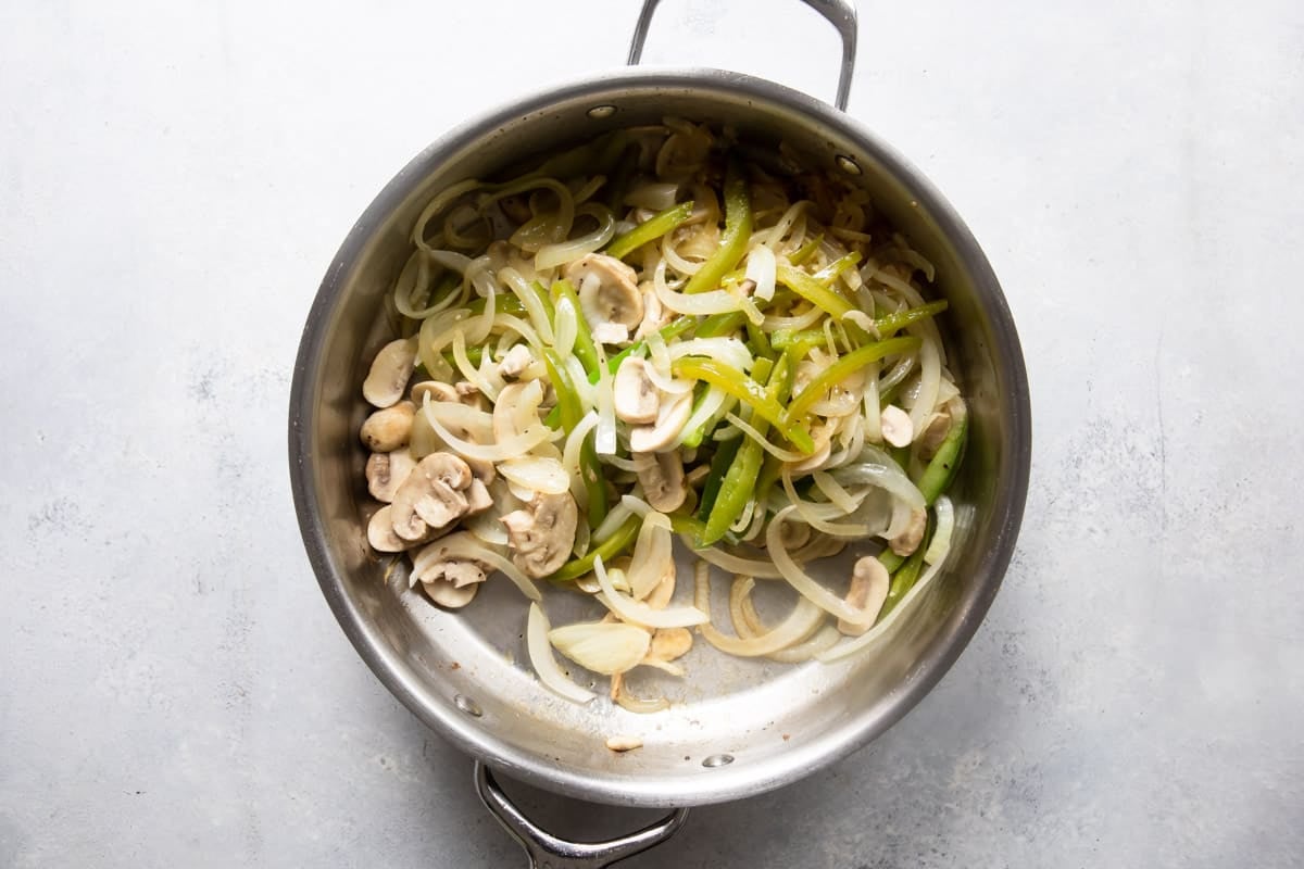 Mushrooms, onions and peppers being cooked in a skillet.