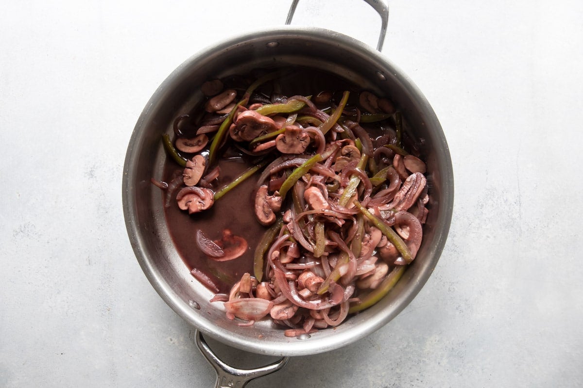 Mushrooms, onions and peppers being cooked in a skillet with wine.
