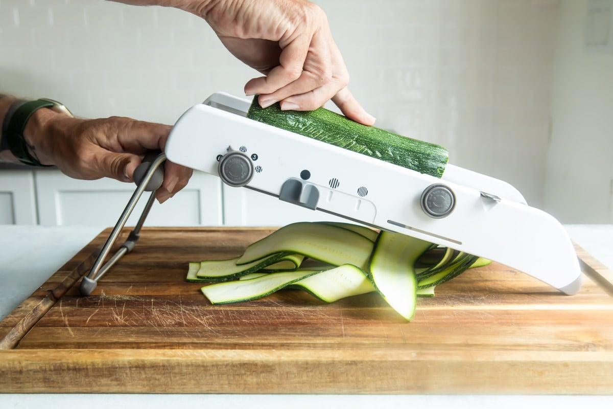 Someone slicing a zucchini on a mandoline.