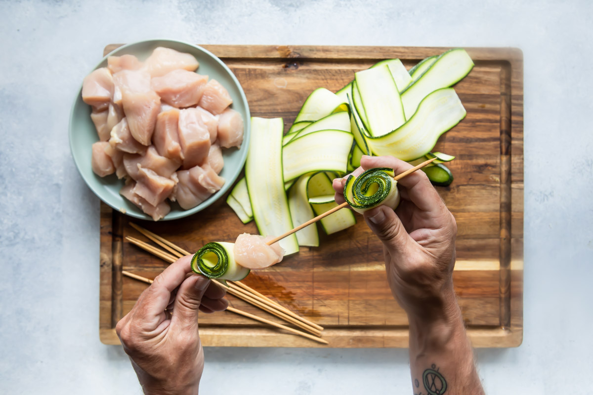 Chicken kabobs being made with chunks of chicken and zucchini rolls.