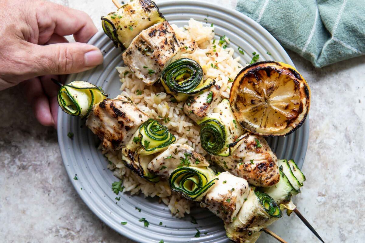 A plate with two chicken kabobs and rice.