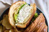A chicken salad sandwich on a croissant with chips next to it.
