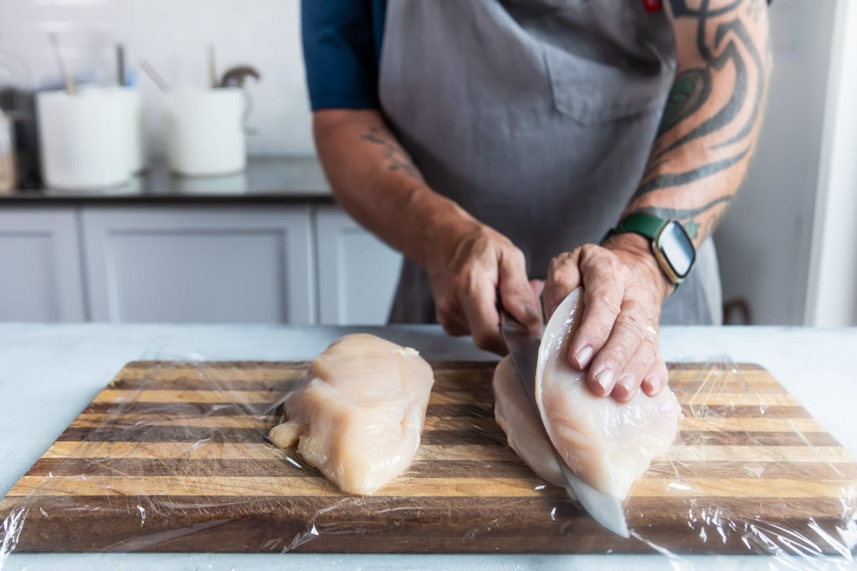 Chicken breasts being butterflied on a wooden cutting board.