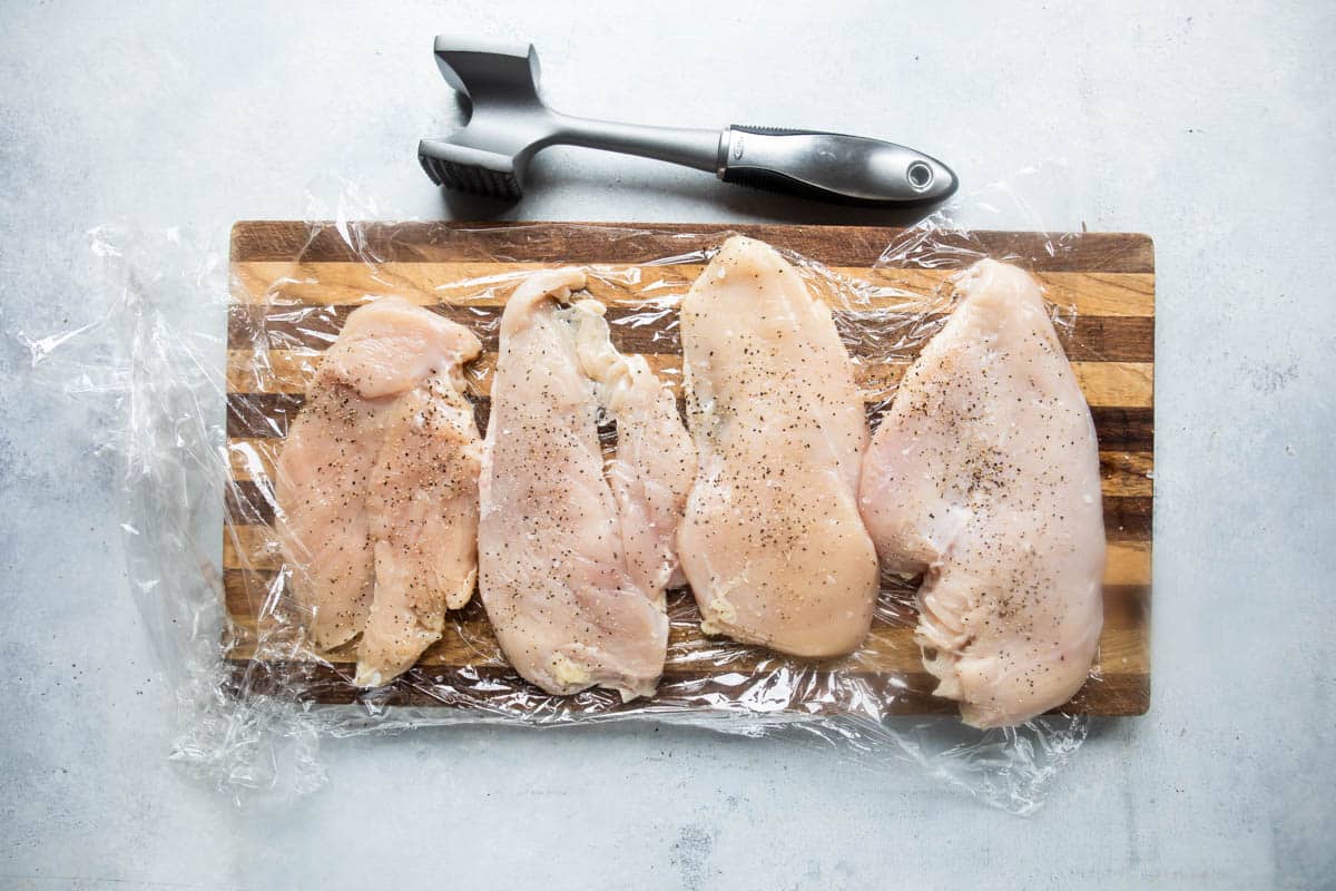 Butterflied chicken breasts on a wooden cutting board after being tenderized.
