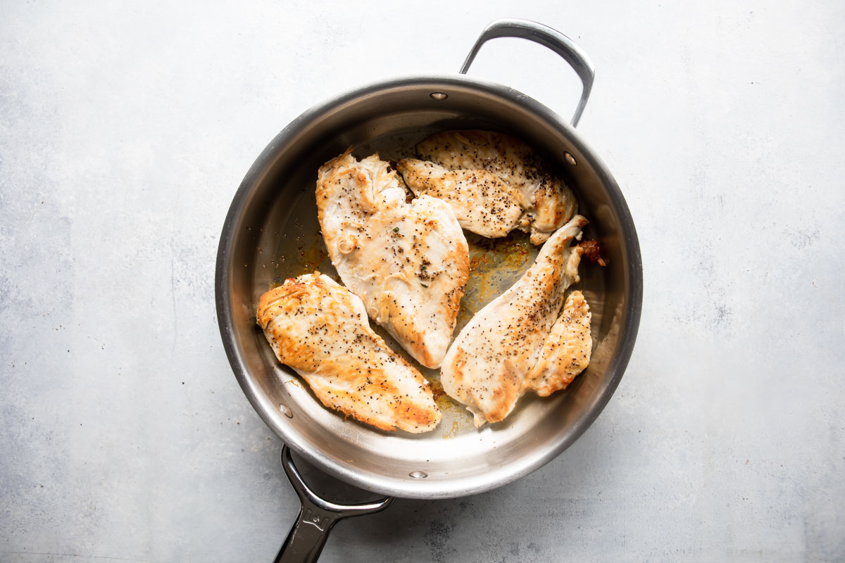 Chicken breasts being cooked in a skillet.