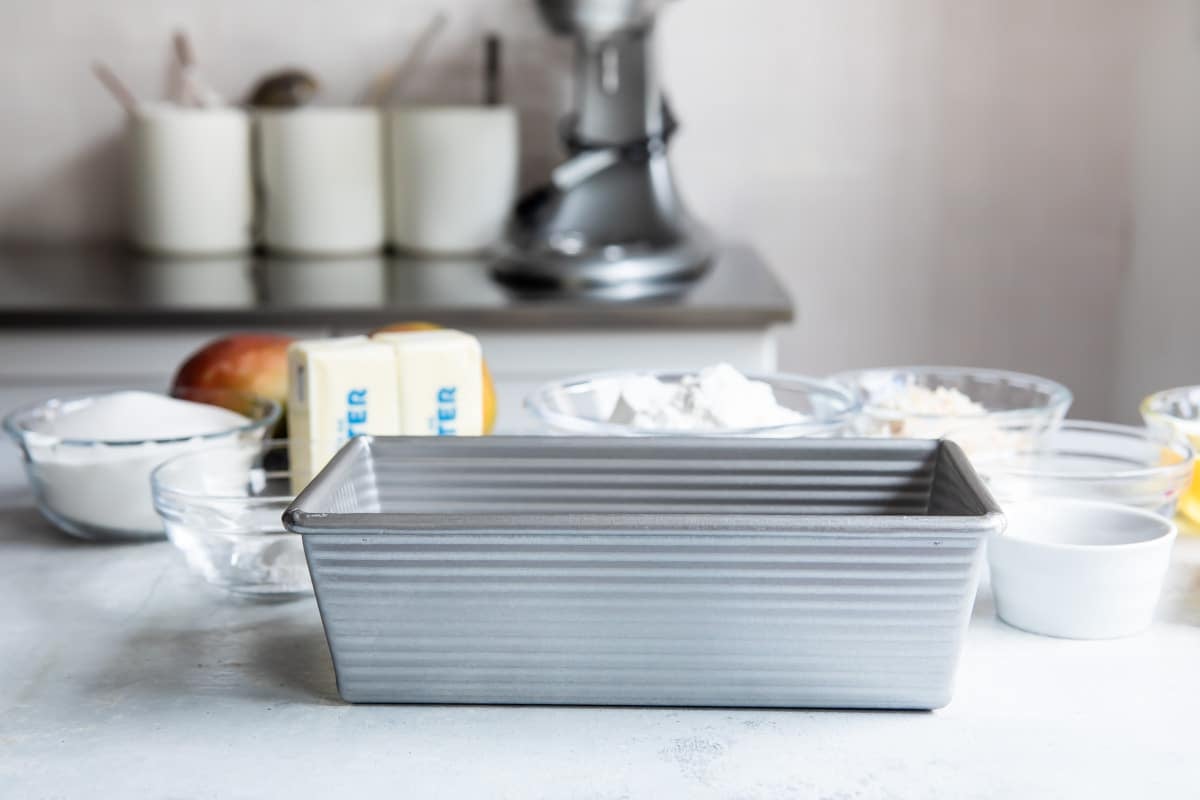 A loaf pan on a countertop surrounded by baking ingredients.