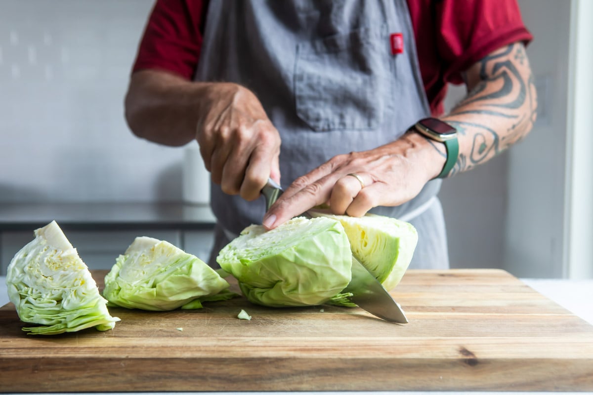 Someone quartering a cabbage on a wooden cutting board.