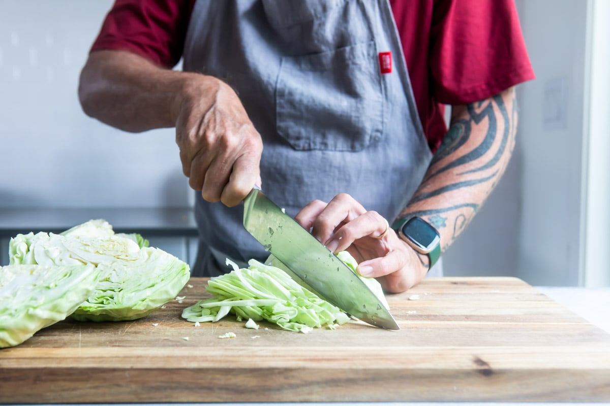 Someone slicing a quarter of a cabbage on a wooden cutting board.