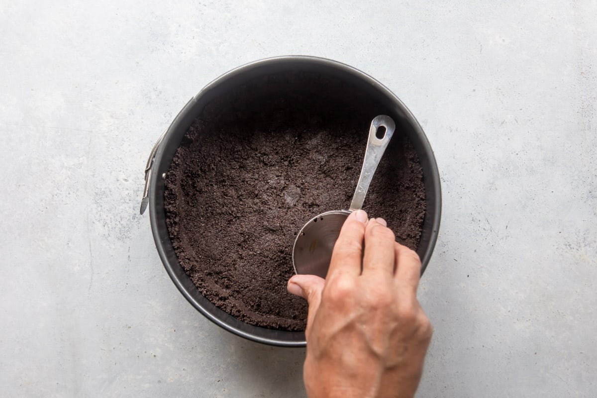 Someone pushing down Oreo crumbs into a springform pan.