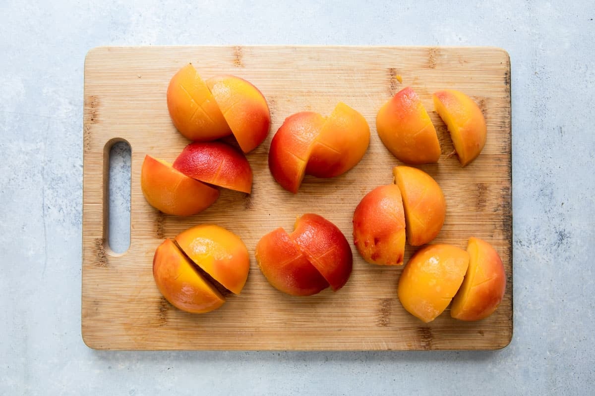 Peeled, halved peaches on a wooden cutting board.