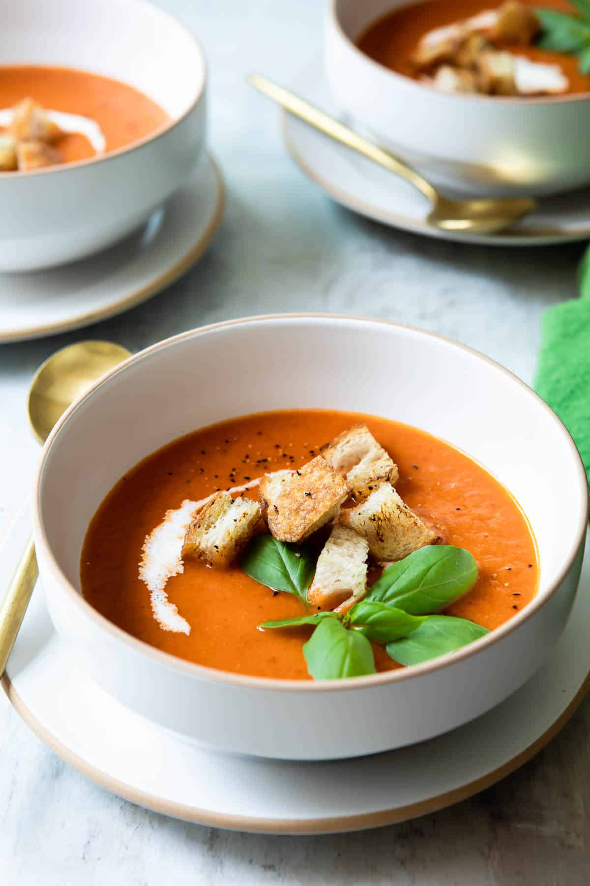 A bowl of roasted tomato soup garnished with basil and croutons.