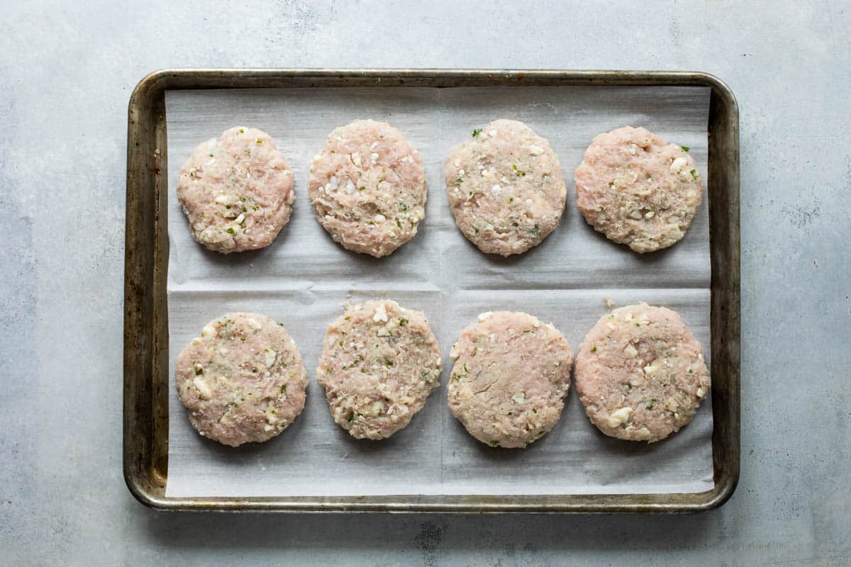Turkey burgers on a parchment paper lined baking sheet before being cooked.