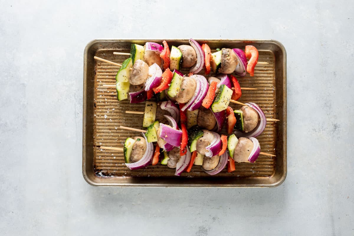 Veggie kabobs on a baking sheet ready to be grilled.