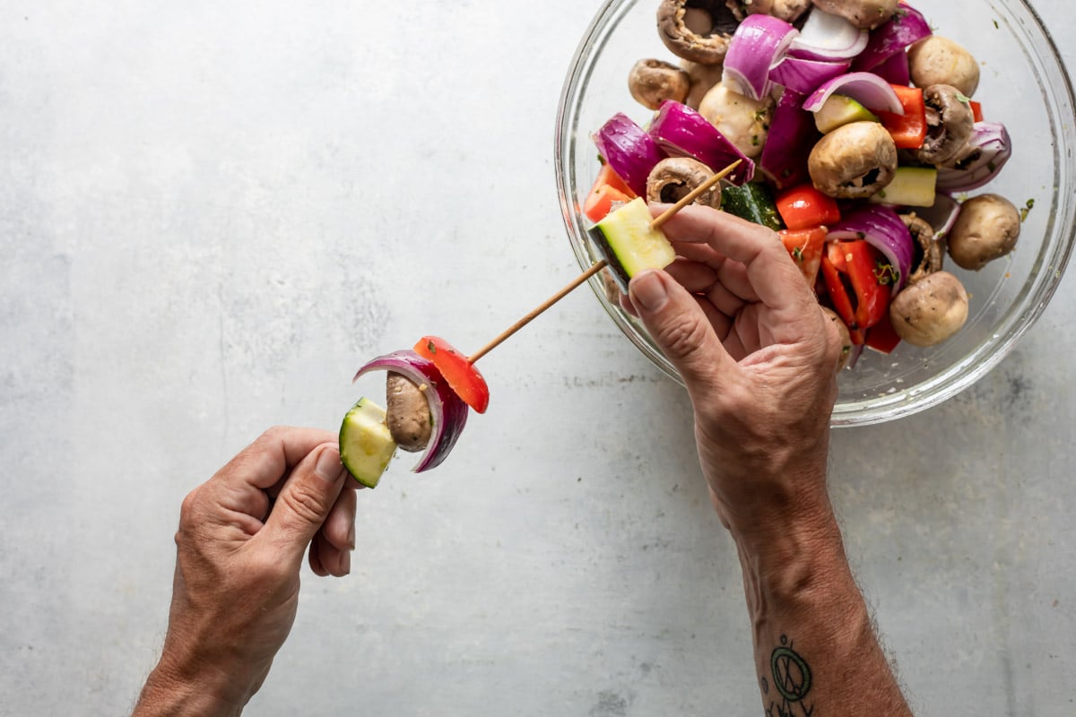 Someone putting vegetables on kabob skewers for veggie kabobs.
