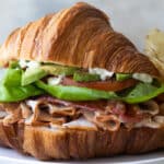A croissant sandwich on a plate with potato chips.