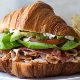 A croissant sandwich on a plate with potato chips.