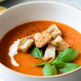 A bowl of roasted tomato soup garnished with basil and croutons.