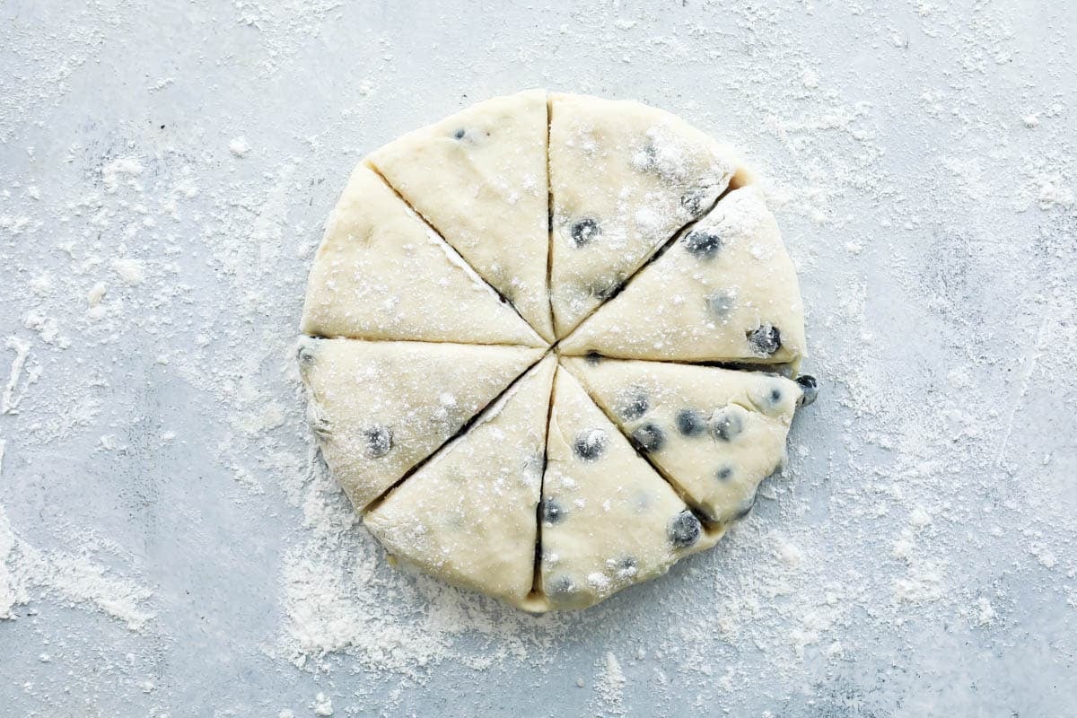 A round piece of blueberry scone dough cut into eight triangles.