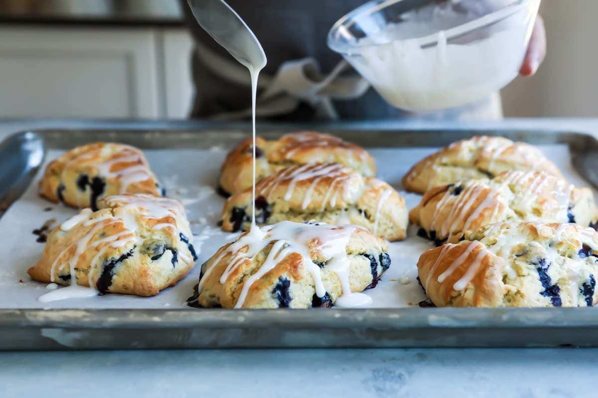 Blueberry scones getting drizzled with icing.