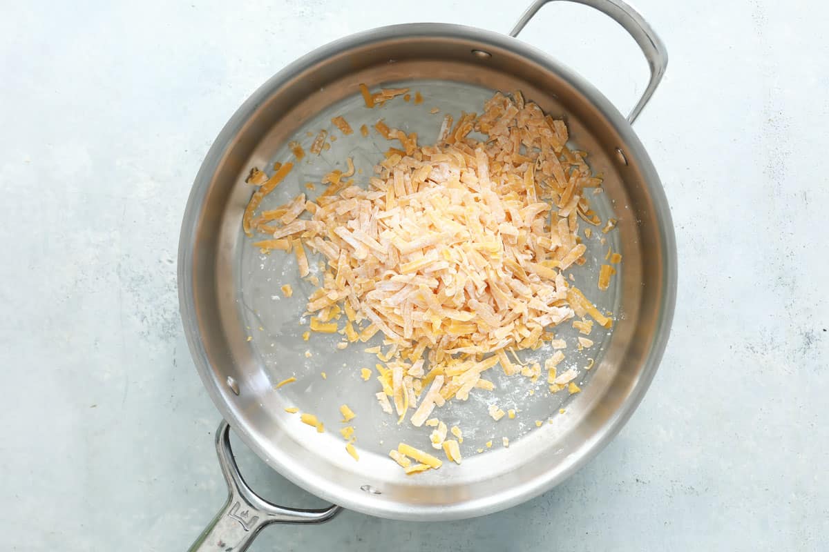 Shredded cheese tossed with cornstarch in a skillet.