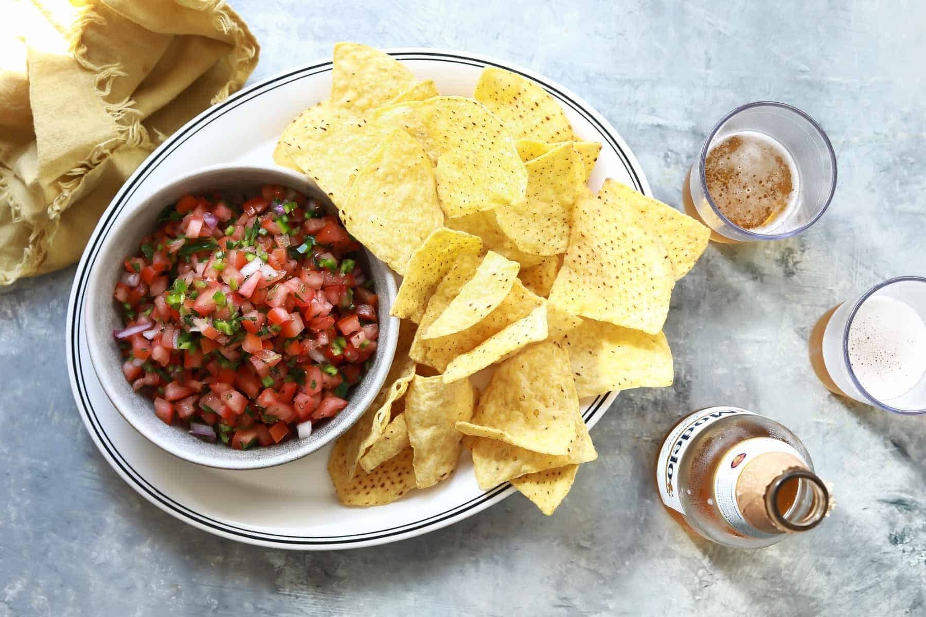 A bowl of pico de gallo on a plate with tortilla chips.