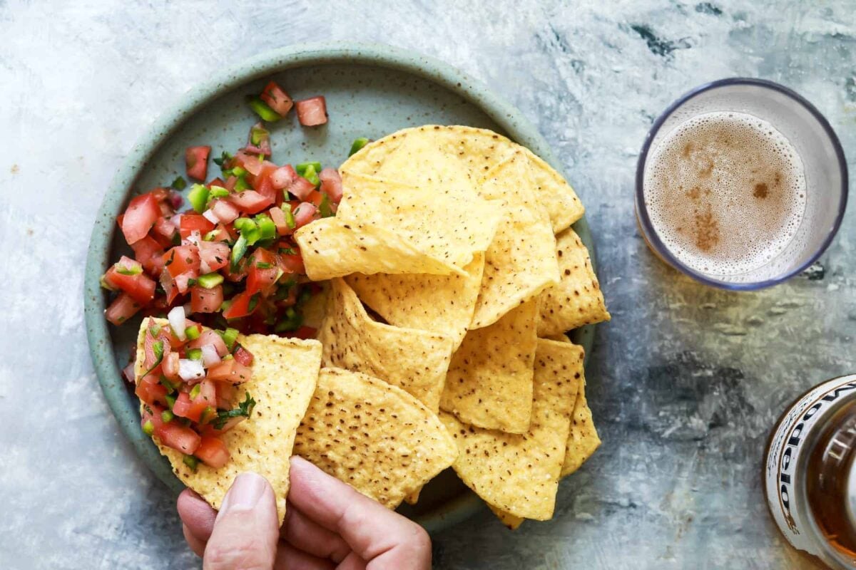Someone scooping pico de gallo with a tortilla chip.
