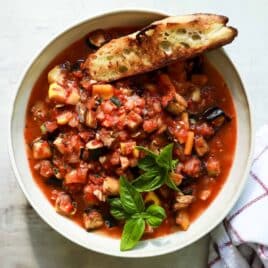 A bowl full of ratatouille stew with grilled bread on the side.