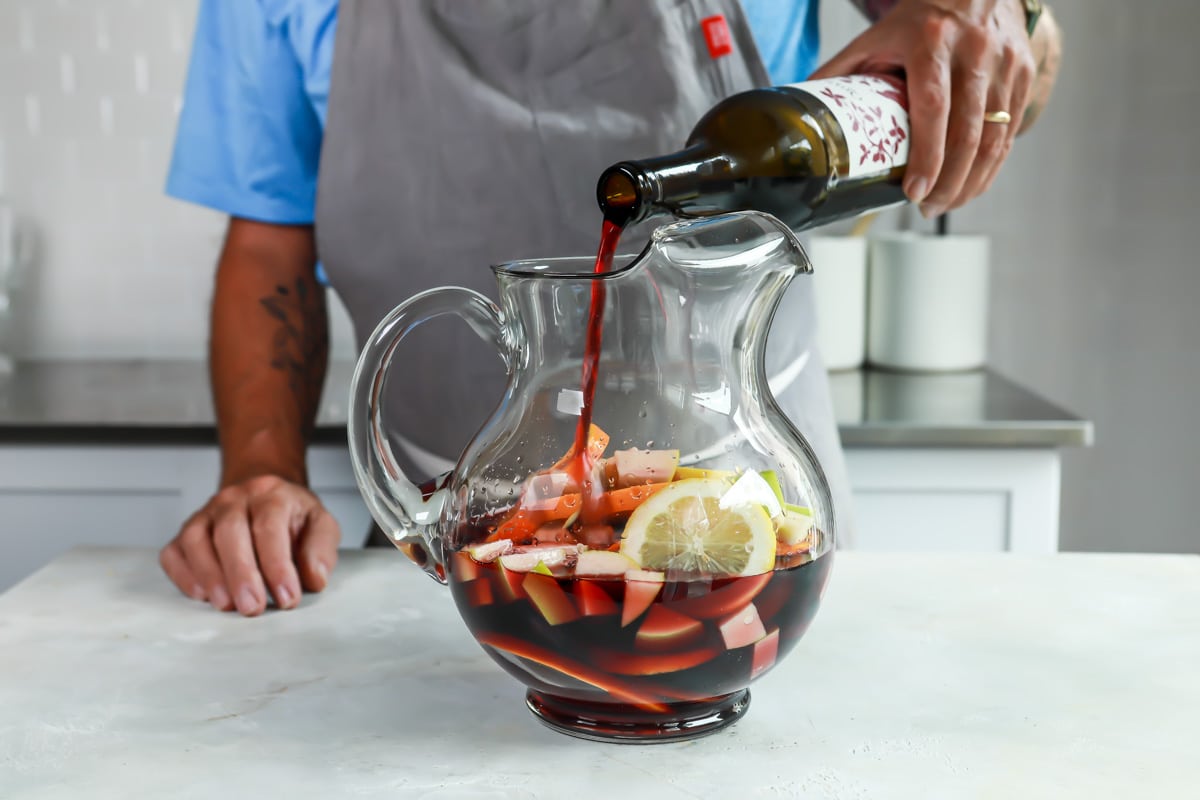 Someone pouring red wine into a glass pitcher.