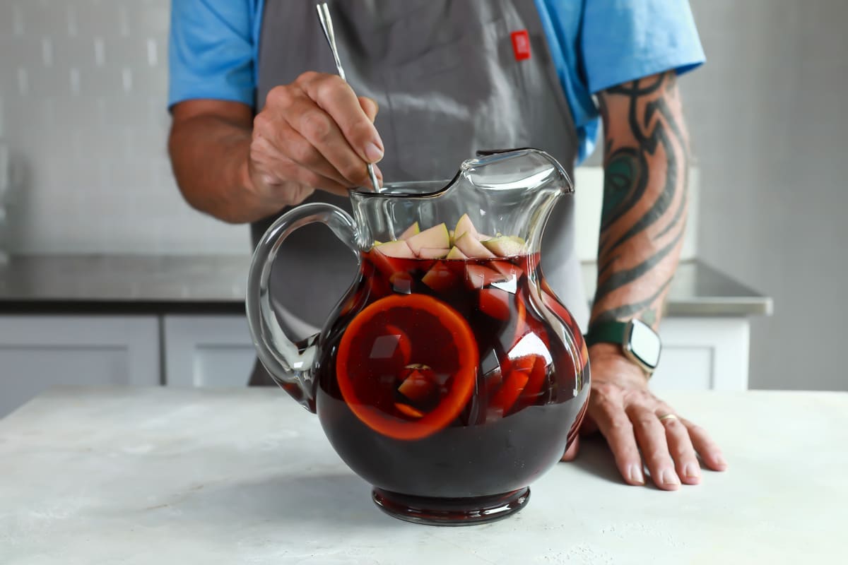 Someone stirring a glass pitcher of red sangria.