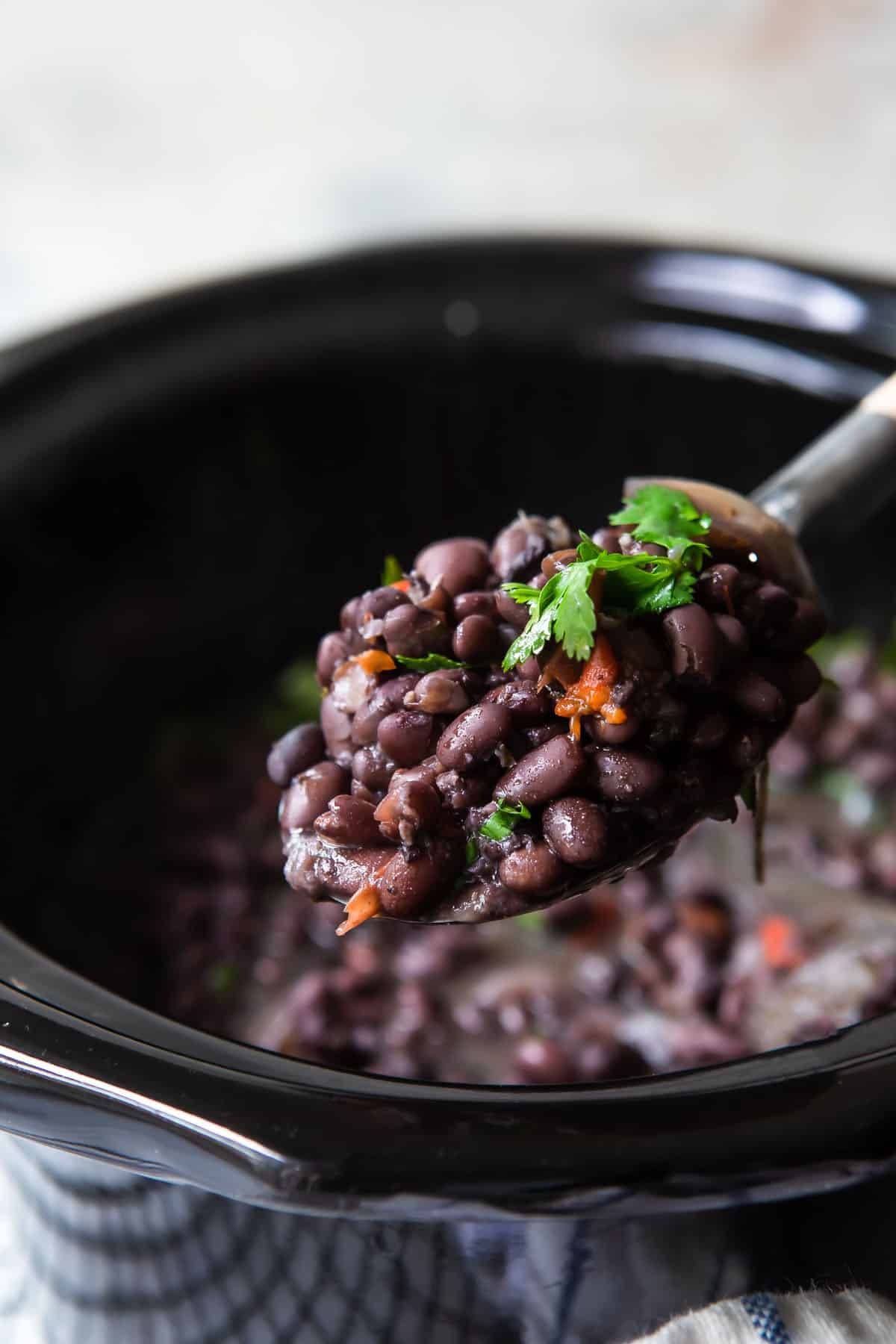 Slow cooker black beans being scooped out of a slow cooker.