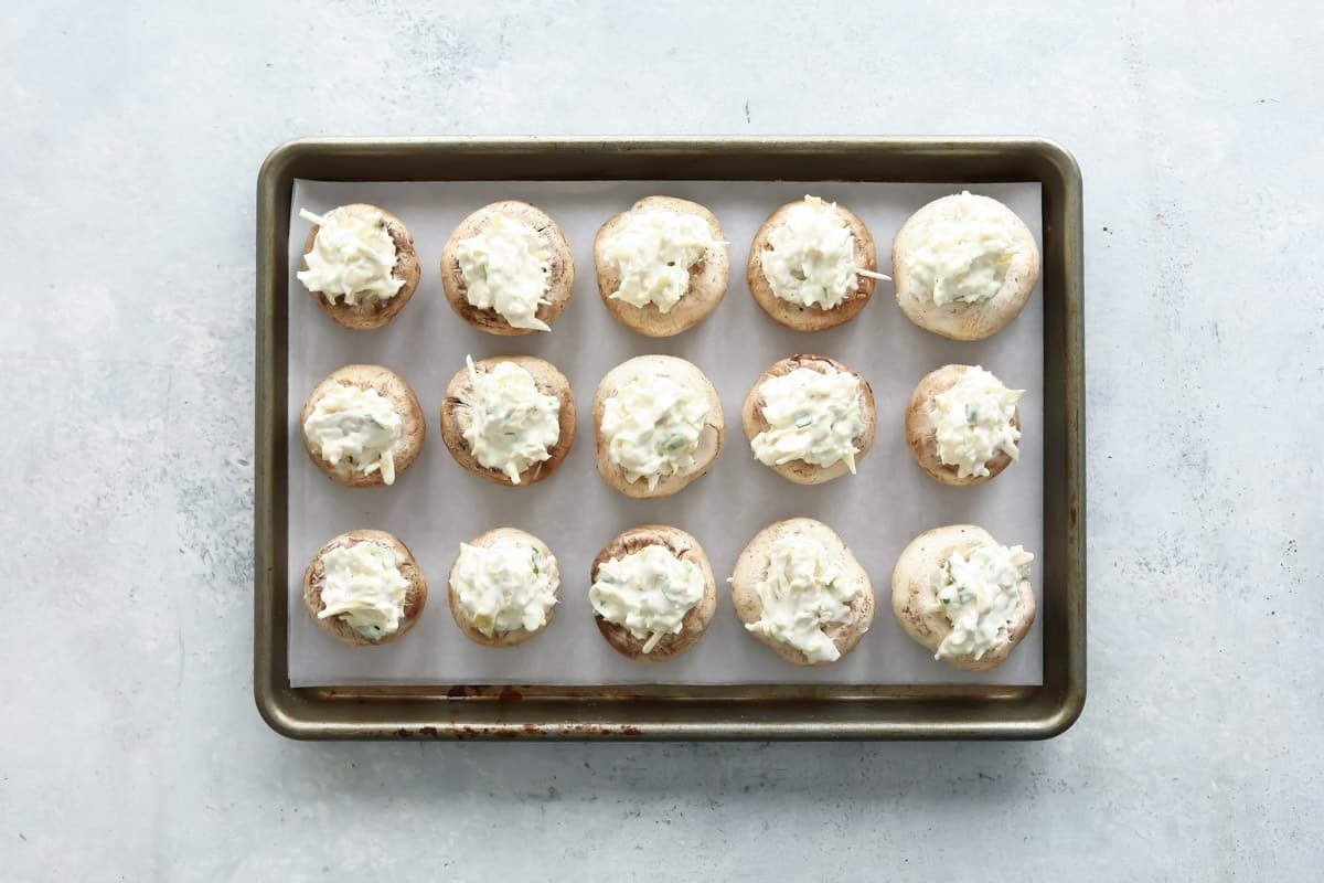 A baking sheet full of unbaked stuffed mushrooms.