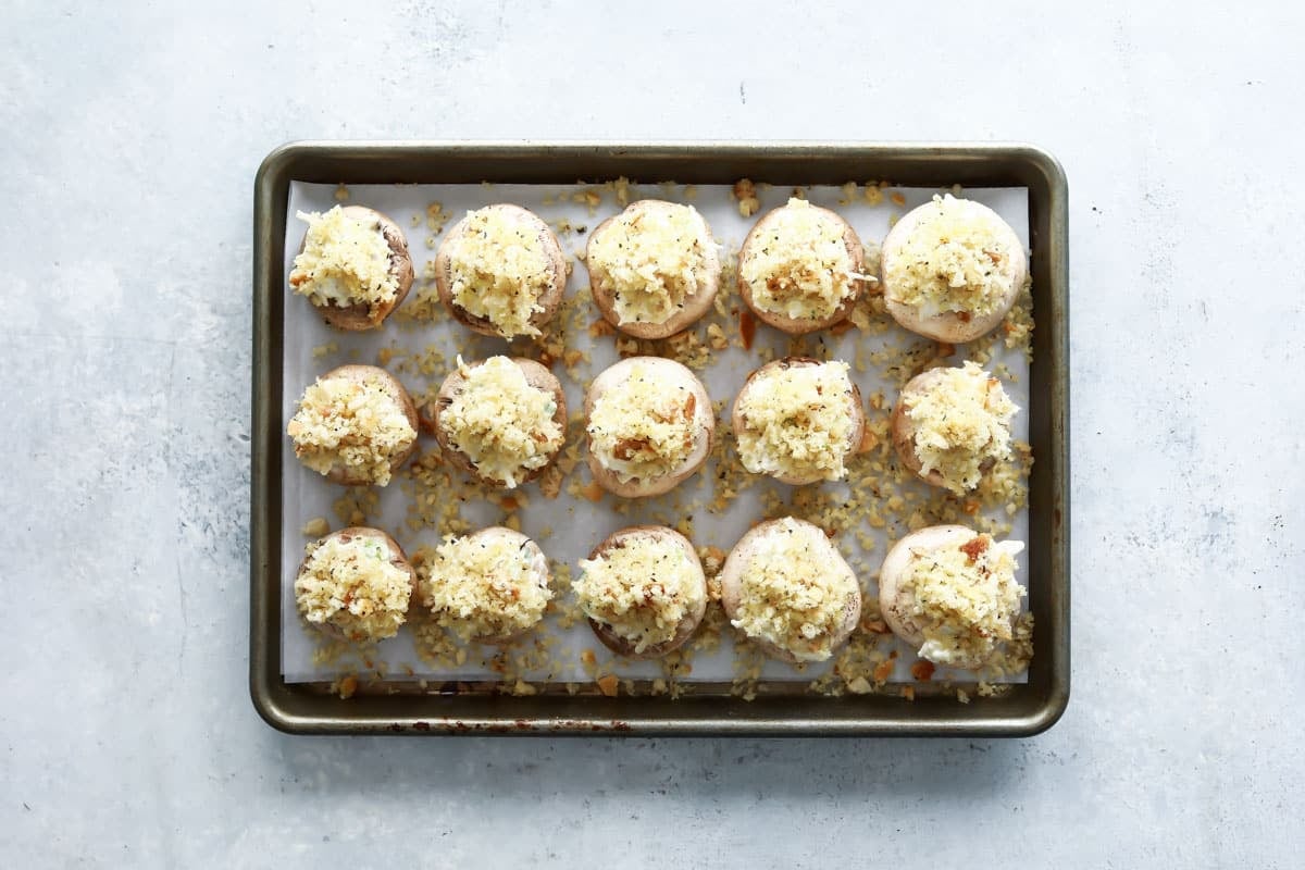 A baking sheet full of unbaked stuffed mushrooms.