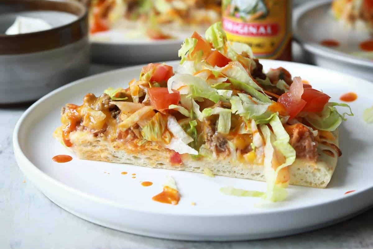 A slice of taco pizza on a white plate.