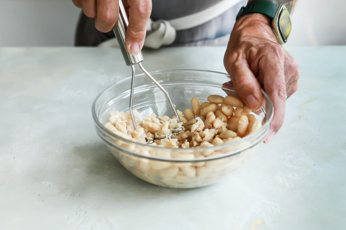 Mashing white beans in a bowl.