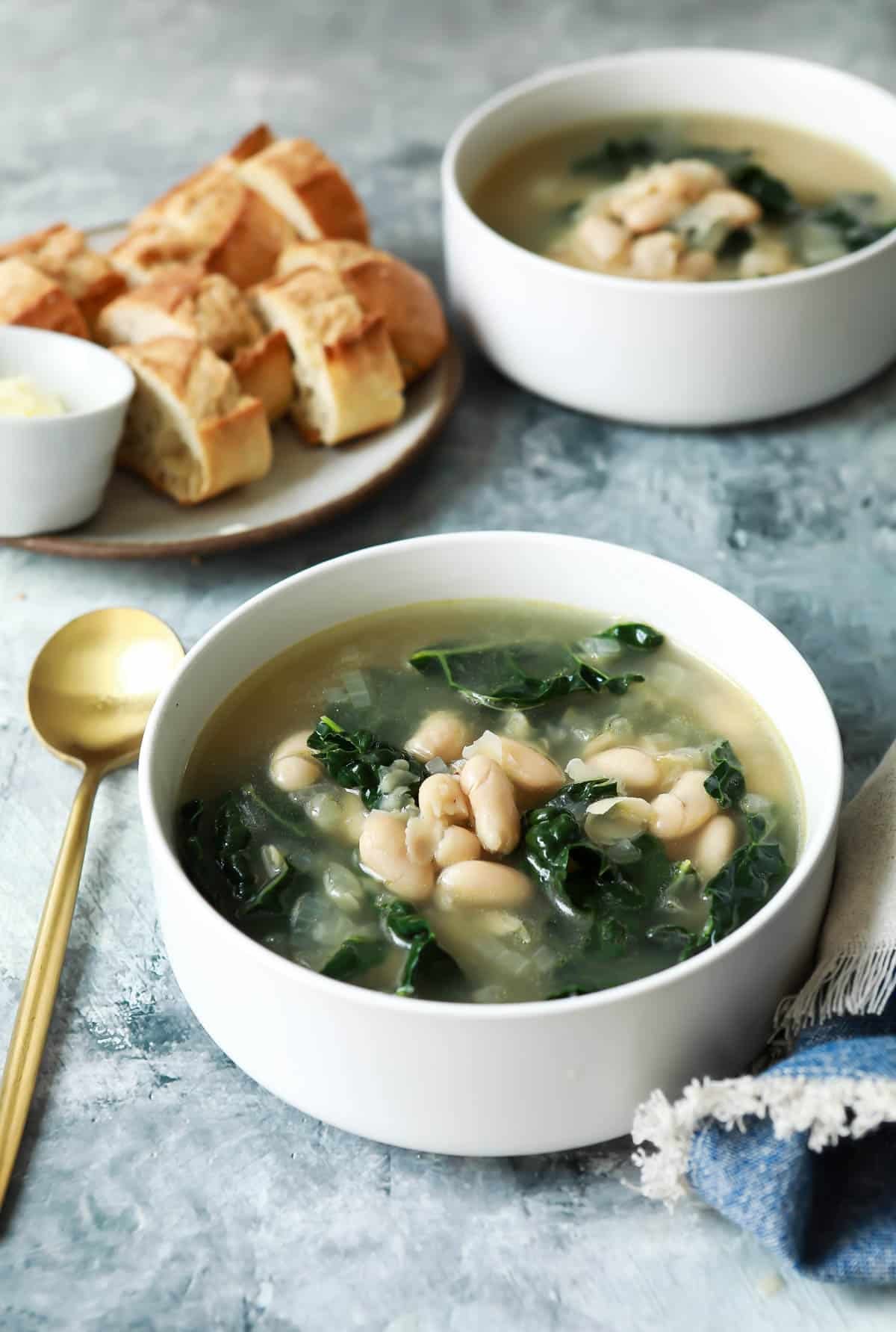 Bowls of white bean and kale soup with crusty bread for serving.