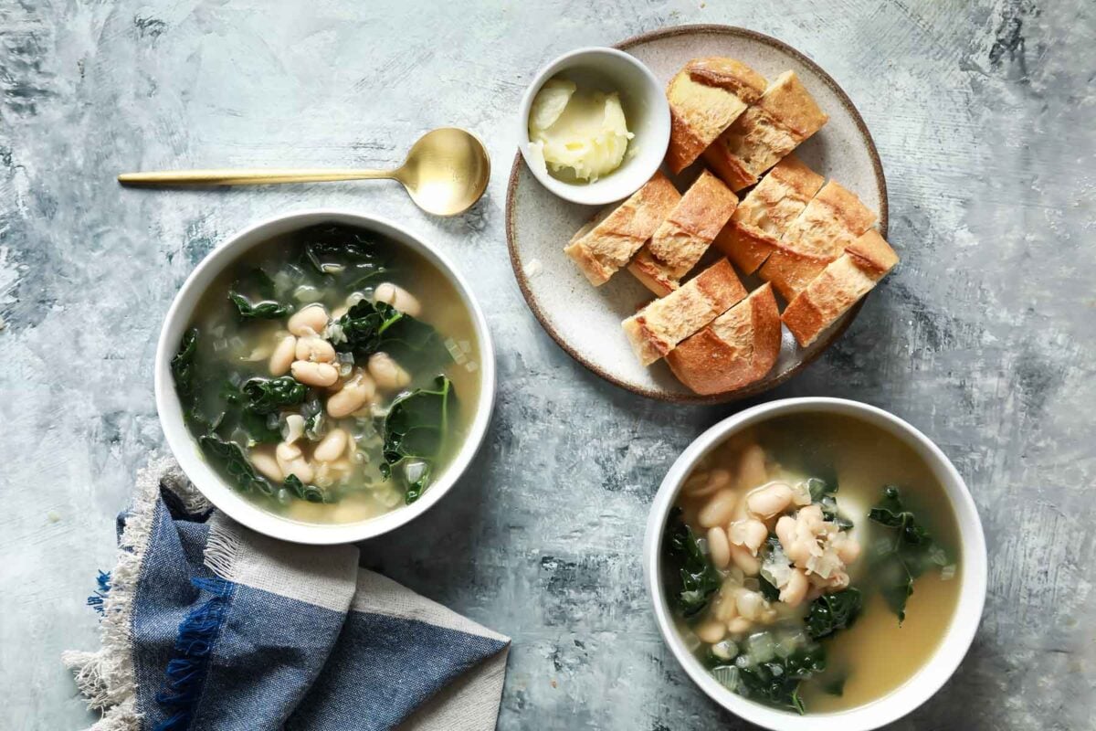 Bowls of white bean and kale soup with crusty bread for serving.