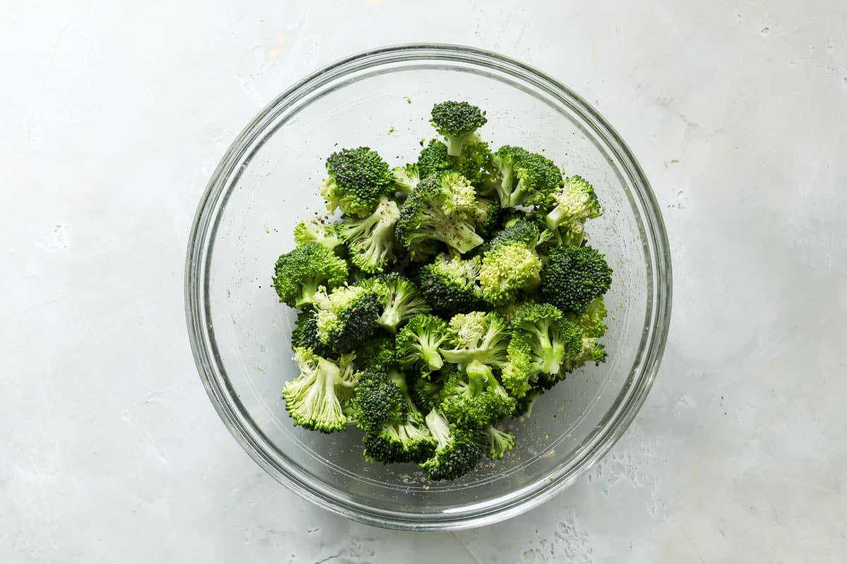 Broccoli in a bowl after being tossed with oil and seasonings.