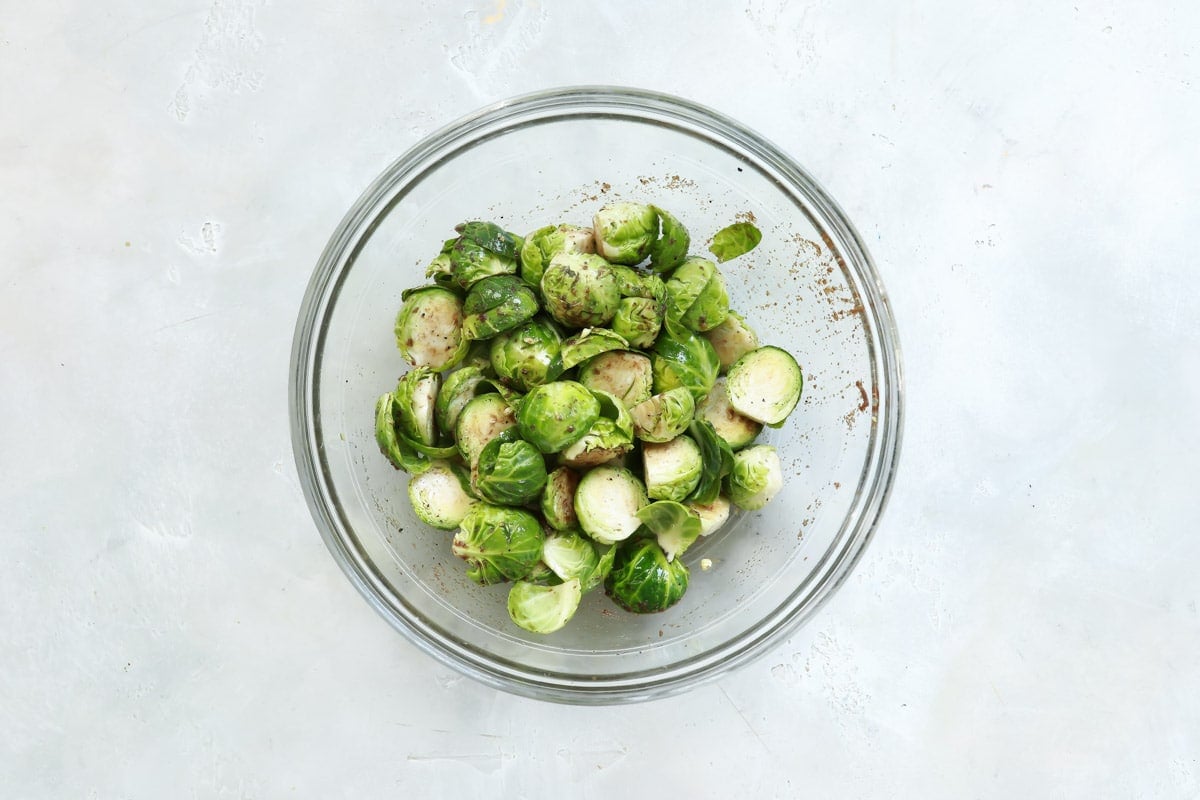 Brussels sprouts in a bowl after being tossed with oil and seasonings.