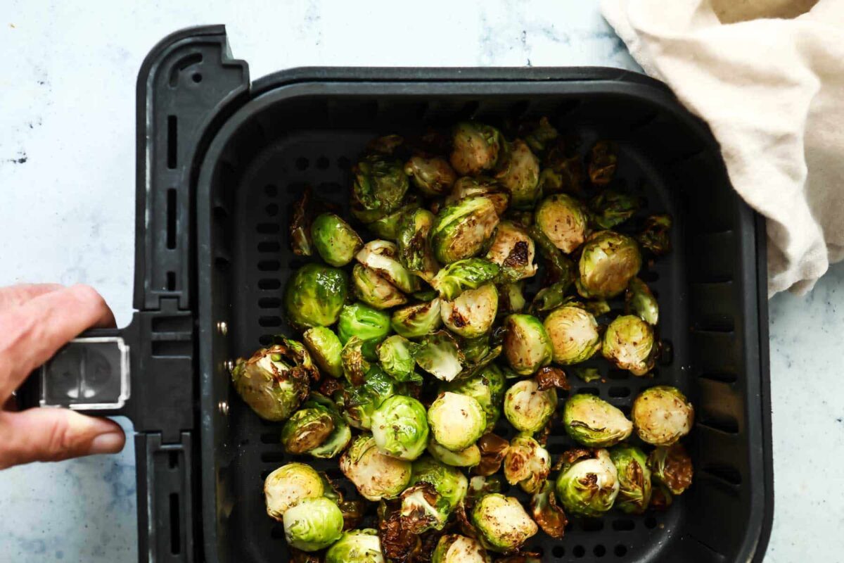 An air fryer basket with Brussels sprouts after being cooked.