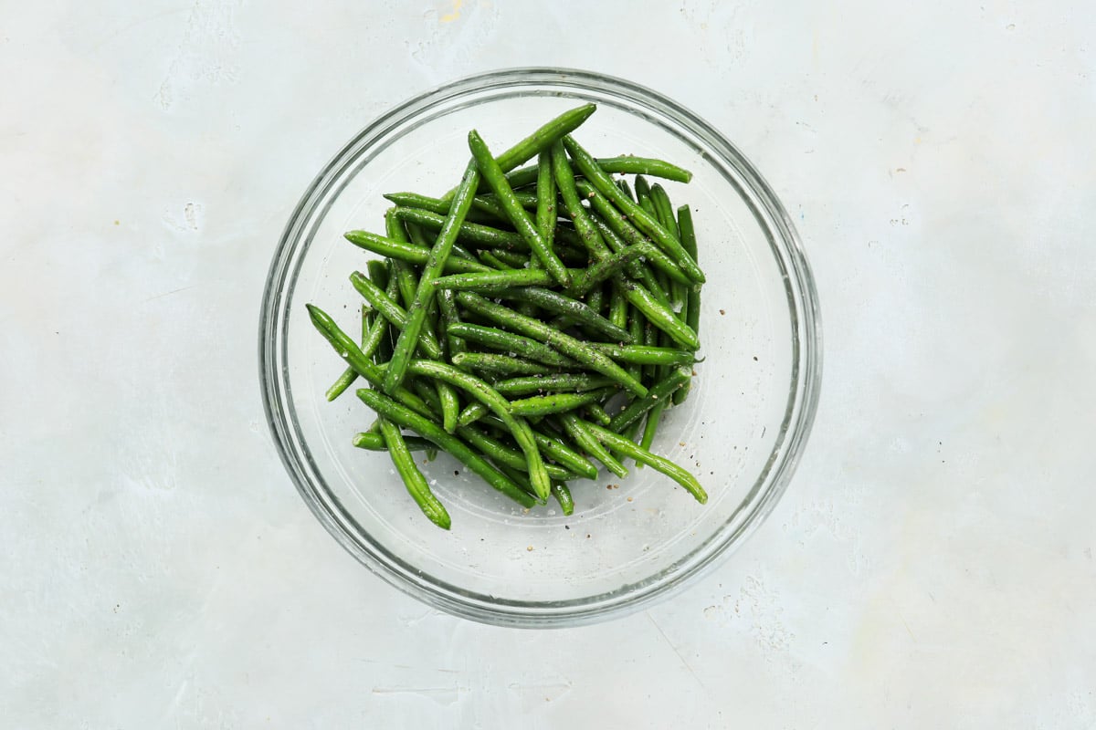Green beans in a bowl after being tossed with oil and seasonings.