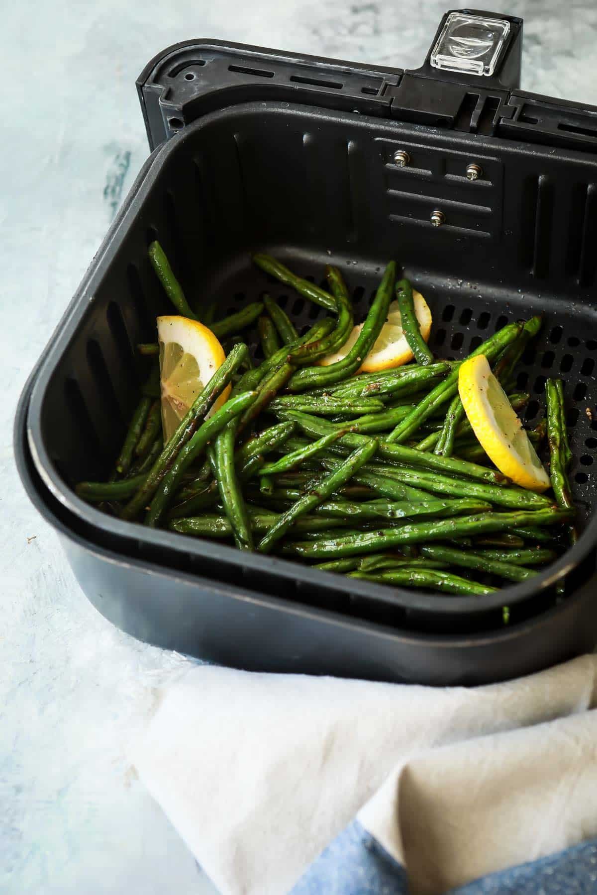 An air fryer basket with green beans after being cooked.