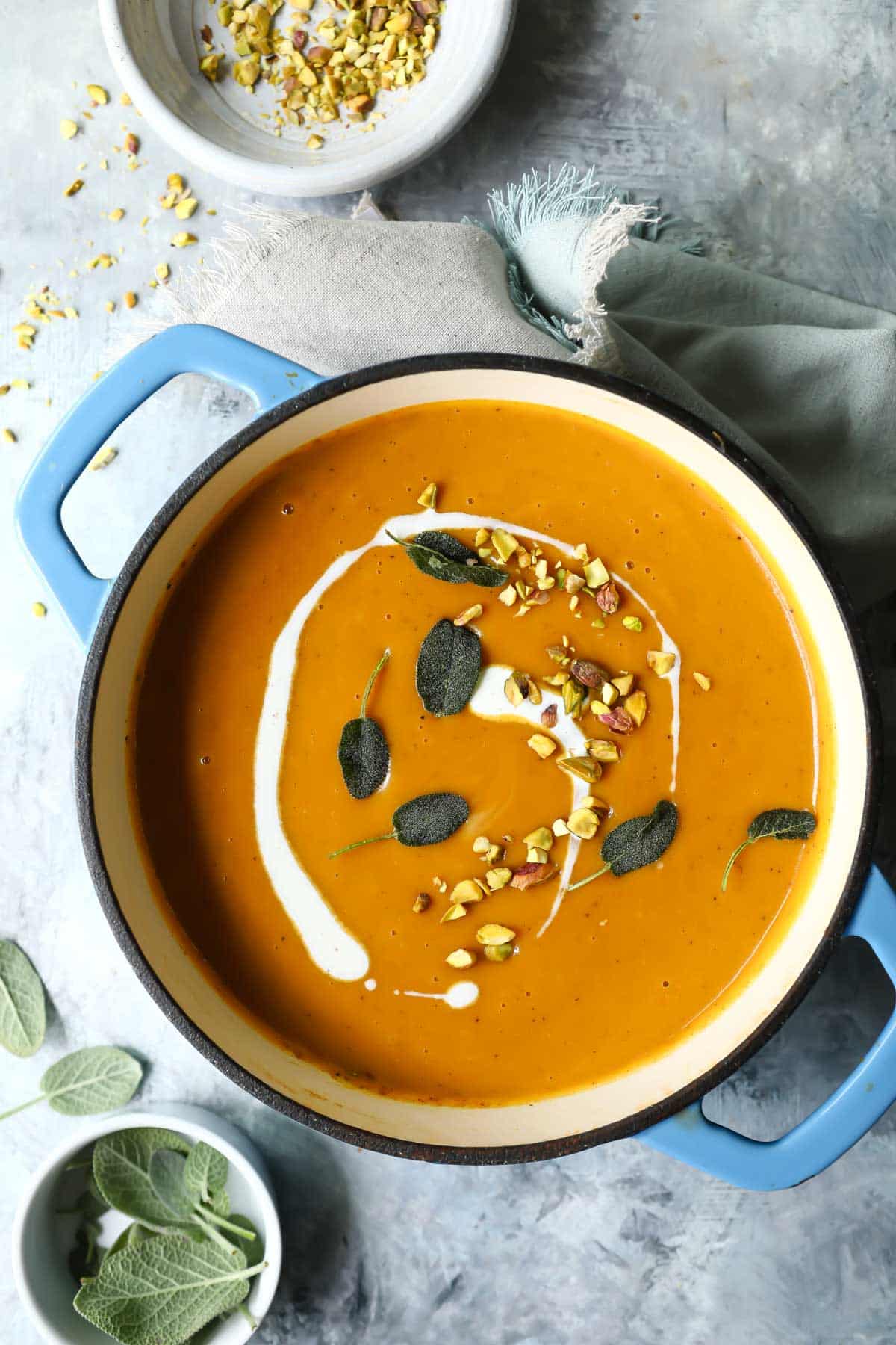 butternut squash soup in dutch oven with drizzle of half and half, garnished with crispy sage leaves and chopped pistachios. 