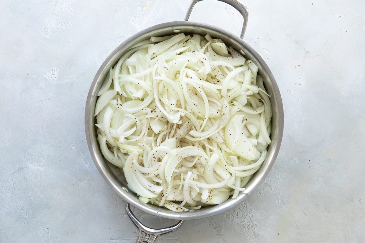 Onions in a silver skillet before being caramelized.