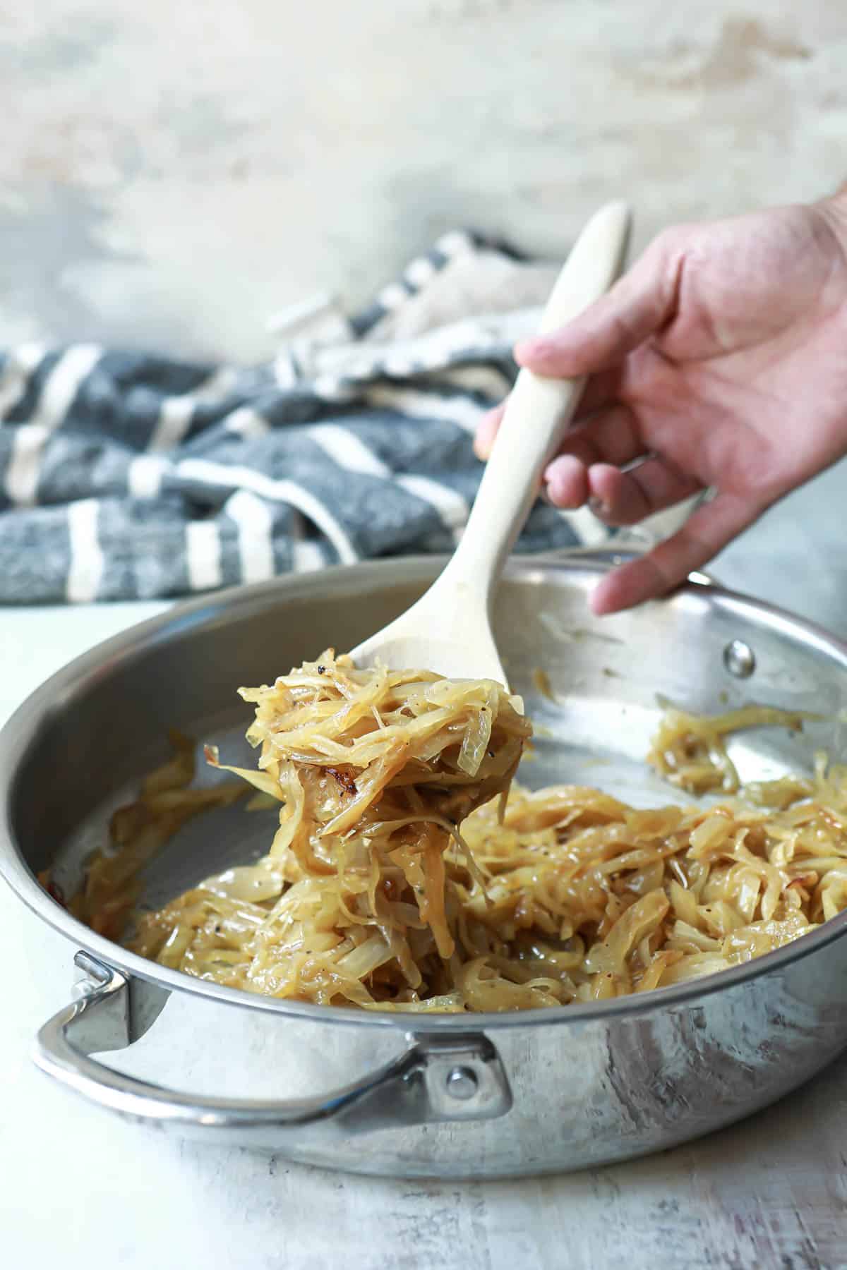 Someone scooping out a spoonful of caramelized onions out of a metal skillet.
