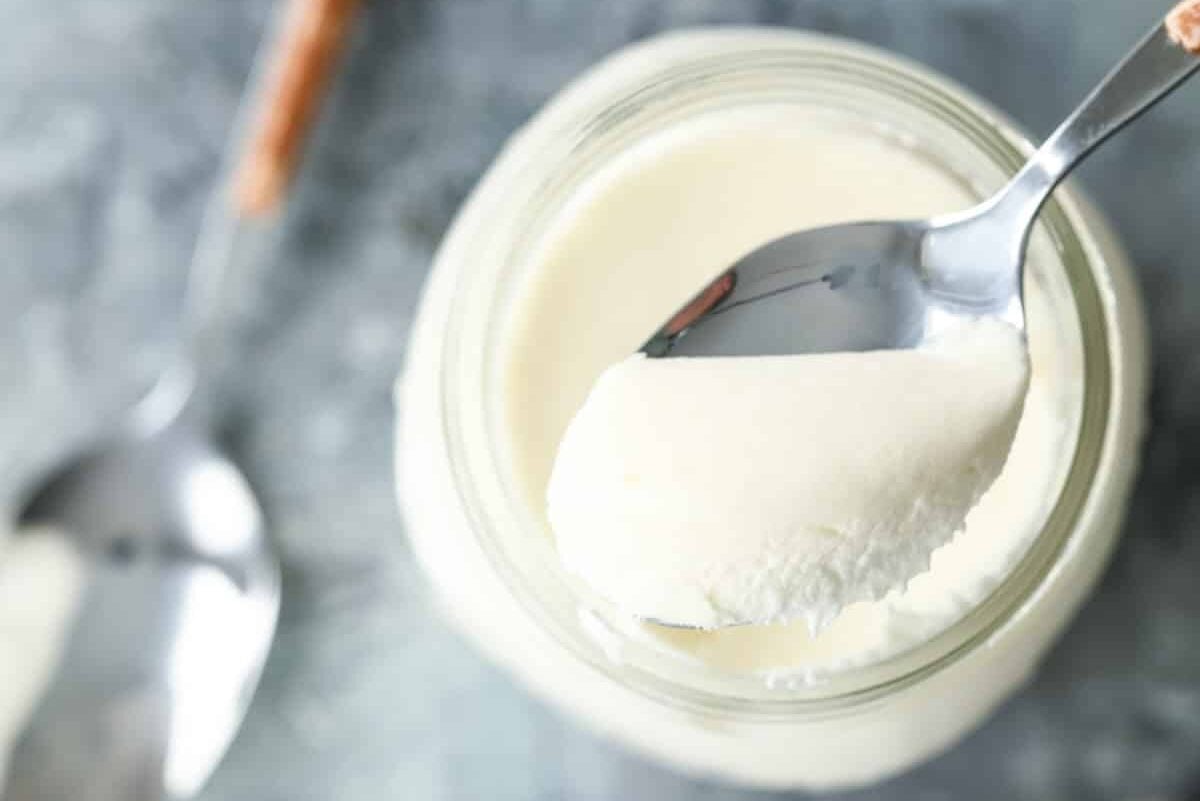 A spoonful of Creme Fraiche being held over a mason jar of creme fraiche.