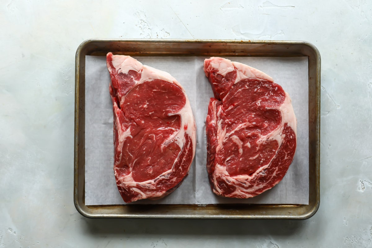 Two rib eyes on a baking sheet before being cooked.