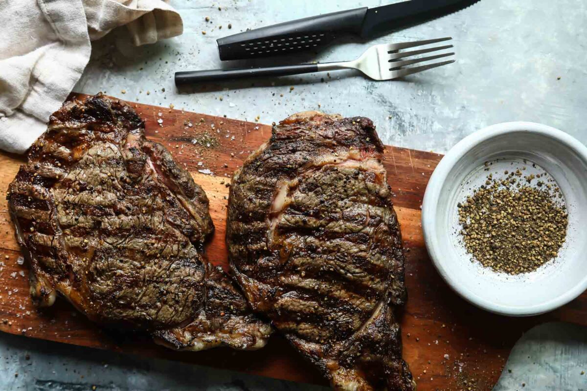 Two Rib Eye steaks on a wooden cutting board.